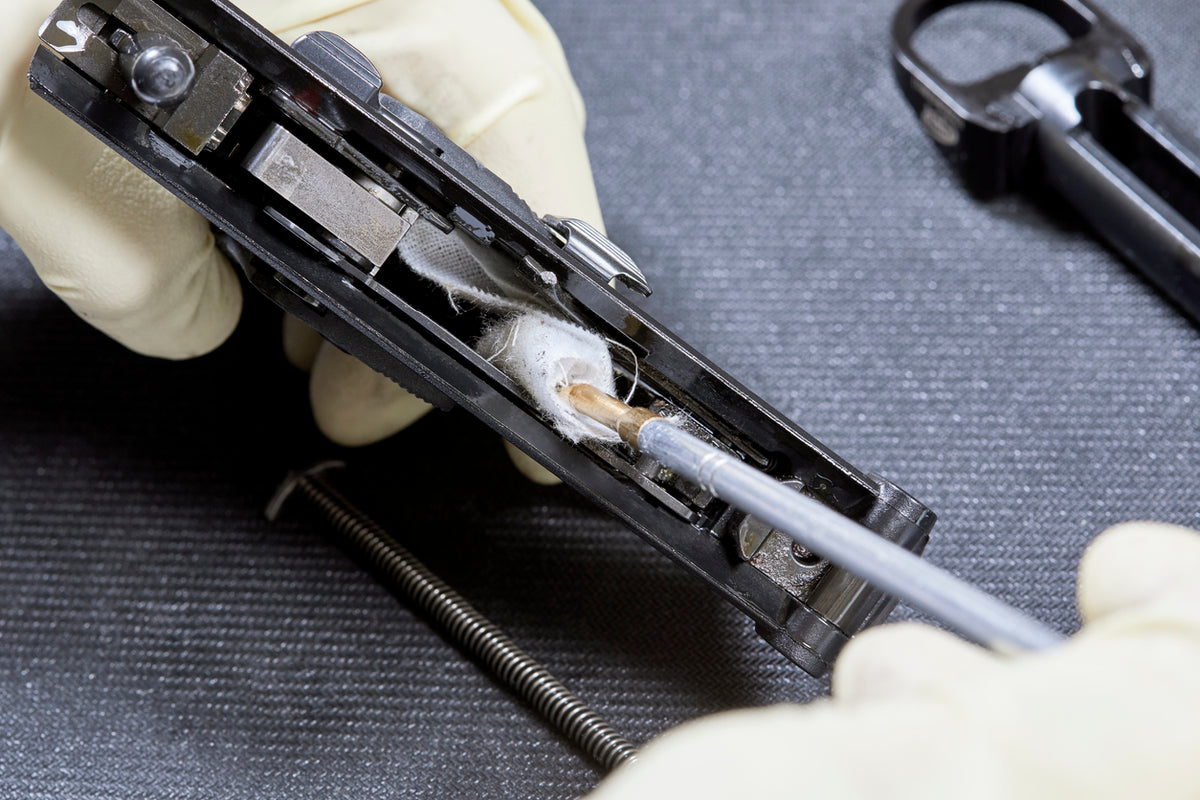 Close-up of a person working on a gun with tools and parts.
