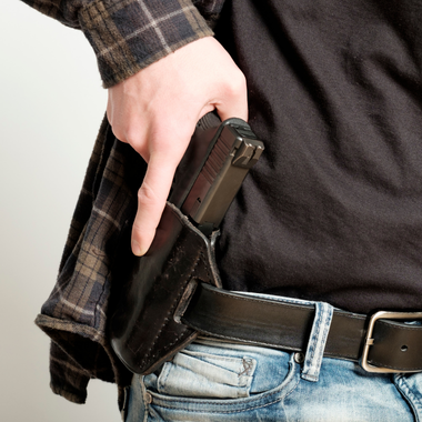 Person drawing a gun from a holster on a plain background