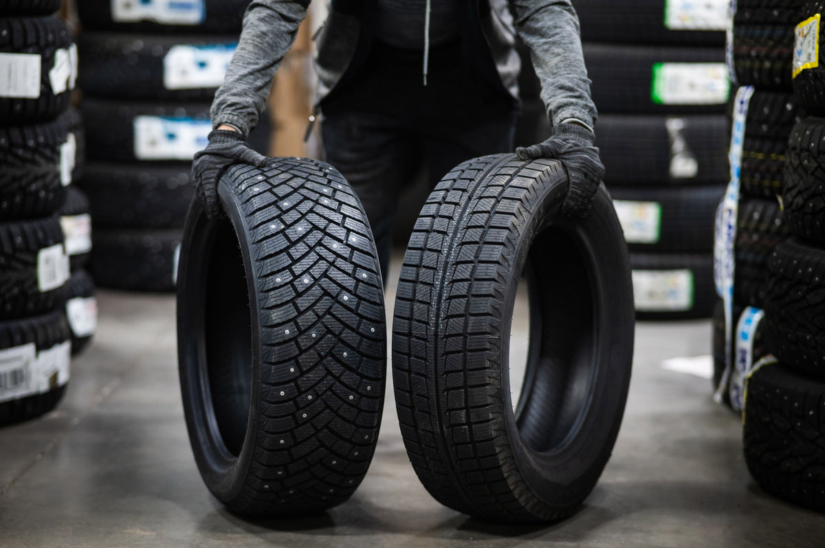 Person holding two tires in a warehouse setting with stacked tires in the background